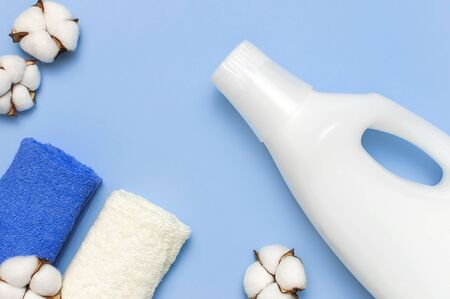 White plastic packaging of laundry detergent, liquid powder, washing conditioner, towels and cotton flowers on blue background. Flat lay top view copy space. Bio organic product. Eco cleaning concept.の写真素材