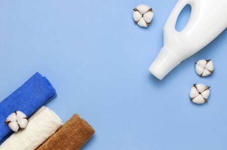 White plastic packaging of laundry detergent, liquid powder, washing conditioner, towels and cotton flowers on blue background. Flat lay top view copy space. Bio organic product. Eco cleaning concept.の写真素材