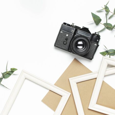 White photo frame old retro camera notebook diary green eucalyptus leaves on white background. Flat lay top view copy space. Stylish minimal composition artwork mockup picture frame home decoration.の写真素材