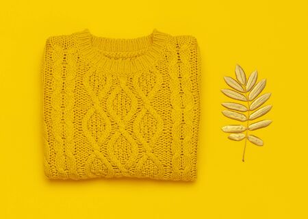 Autumn flat lay composition. Orange yellow knitted woolen female sweater and golden leaves on yellow background top view. Fashionable women's fall accessories. Cozy Knit Jumper Stylish Lady Clothes.の写真素材