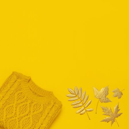 Autumn flat lay composition. Orange yellow knitted woolen female sweater and golden leaves on yellow background top view. Fashionable women's fall accessories. Cozy Knit Jumper Stylish Lady Clothes.の写真素材