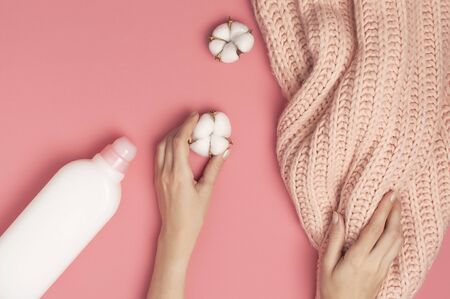 Eco cleaning concept. White plastic packaging of laundry detergent, liquid powder, washing conditioner, knitted wool sweater, cotton flowers on pink background. Flat lay top view. Bio organic product.の写真素材
