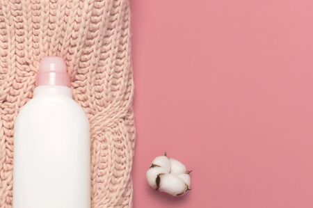 Eco cleaning concept. White plastic packaging of laundry detergent, liquid powder, washing conditioner, knitted wool sweater, cotton flowers on pink background. Flat lay top view. Bio organic product.の写真素材