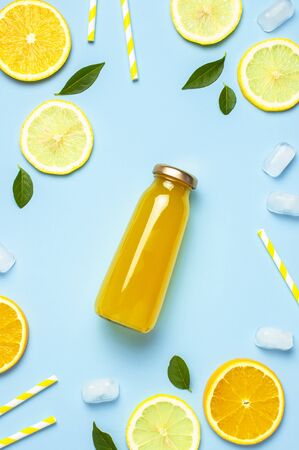 Flat lay composition with glass bottles of juice or fresh, slices of fresh lemon and orange, green leaves, ice cubes on blue background top view copy space. Citrus Juice Concept, Vitamin C, Fruits.の写真素材