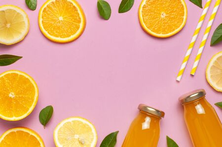 Flat lay composition with glass bottles of juice or fresh, slices of fresh lemon and orange, green leaves, cocktail tubes on pink background top view copy space. Citrus Juice Concept Vitamin C Fruits.の写真素材