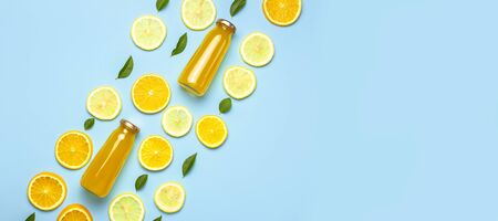 Flat lay composition with glass bottles of juice or fresh, slices of fresh lemon and orange, green leaves, ice cubes on blue background top view copy space. Citrus Juice Concept, Vitamin C, Fruits.の写真素材