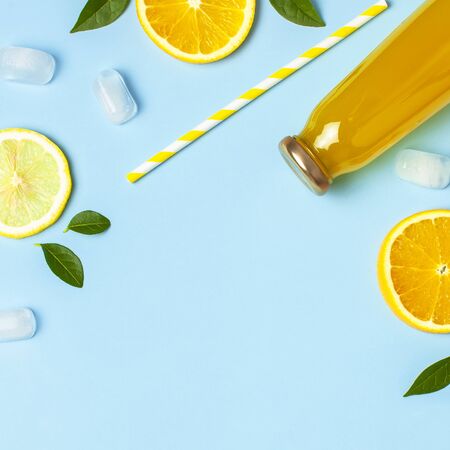 Flat lay composition with glass bottles of juice or fresh, slices of fresh lemon and orange, green leaves, ice cubes on blue background top view copy space. Citrus Juice Concept, Vitamin C, Fruits.の写真素材