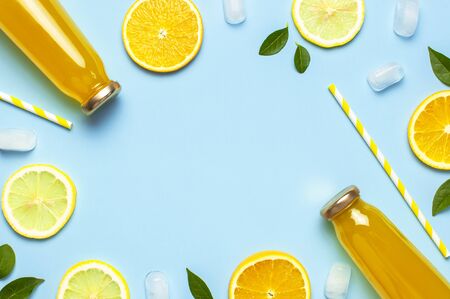 Flat lay composition with glass bottles of juice or fresh, slices of fresh lemon and orange, green leaves, ice cubes on blue background top view copy space. Citrus Juice Concept, Vitamin C, Fruits.の写真素材