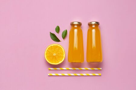 Flat lay composition with glass bottles of juice or fresh, slices of fresh lemon and orange, green leaves, cocktail tubes on pink background top view copy space. Citrus Juice Concept Vitamin C Fruits.の写真素材
