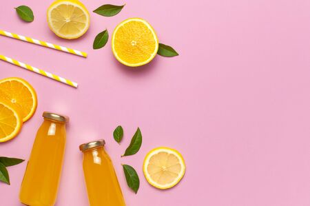 Flat lay composition with glass bottles of juice or fresh, slices of fresh lemon and orange, green leaves, cocktail tubes on pink background top view copy space. Citrus Juice Concept Vitamin C Fruits.の写真素材