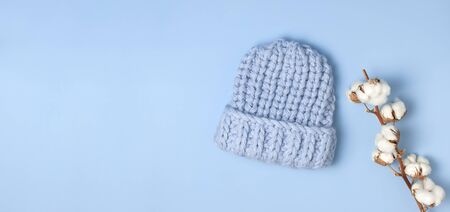 Flat lay fashionable blue knitted winter hat for women, branch of cotton on blue background top view. Stylish woolen hat, concept of winter accessories for the cold. Advertising, shopping, winter sale.の写真素材