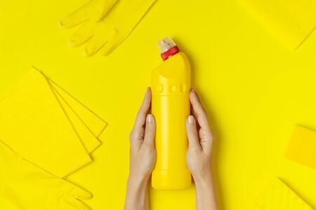 House cleaning concept. Women's hands hold household chemicals disinfectant antibacterial gel yellow rubber gloves sponge rags on yellow background. Flat lay top view copy space. Cleaning accessories.の写真素材