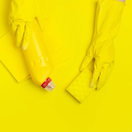 House cleaning concept. Women's hands in yellow rubber gloves, household chemicals, bleach, antibacterial gel, sponge, rags on yellow background. Flat lay top view copy space. Cleaning accessories.の写真素材