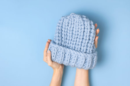 Flat lay fashionable blue knitted winter hat in female hands on blue background top view. Stylish...