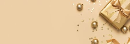 Merry Christmas and Happy Holidays greeting card. Beautiful golden gift with balls and confetti stars on gold background top view Flat lay. New Year presents Festive decorations 2020 celebration.の写真素材