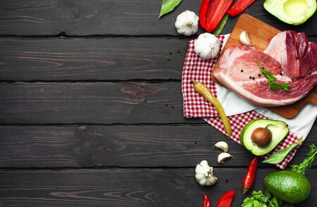 Big fresh piece of meat on cutting board with ingredients for cooking pepper garlic avocado dill parsley on dark wooden background top view. Raw steak from pork or beef. Cooking concept, healthy food.の写真素材