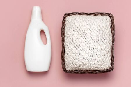 Eco washing concept. White plastic packaging of laundry detergent, liquid powder, washing conditioner, knitted sweater, rattan wicker basket on pink background. Flat lay top view. Bio organic product.の写真素材
