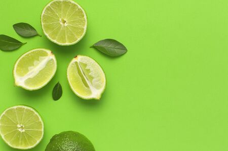 Fresh juicy lime and green leaves on bright green background. Top view flat lay copy space. Creative food background, tropical fruit, vitamin C, citrus. Composition with whole and slices of lime.の写真素材