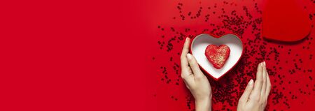 Woman hands holding red gift box shape of heart Heart Shaped Macaroon Cake confetti on red background top view Flat lay. Creative composition for Valentine's Day love concept birthday mother day.の写真素材
