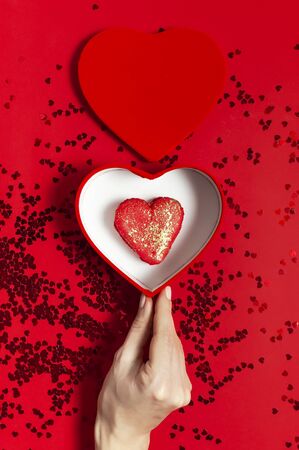 Woman hands holding red gift box shape of heart Heart Shaped Macaroon Cake confetti on red background top view Flat lay. Creative composition for Valentine's Day love concept birthday mother day.の写真素材