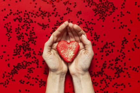 Woman hands holding red Heart Shaped Macaroon Cake and confetti on red background topview Flat lay. Creative composition for Valentine's Day love concept birthday present mother day holiday background.の写真素材