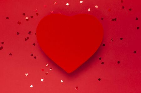 Red gift box in the shape of heart and confetti on red background top view Flat lay. Creative composition for Valentine's Day, love concept, birthday present, mother day, holiday background.の写真素材