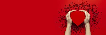 Woman hands holding red gift box shape of heart and confetti on red background top view Flat lay. Creative composition for Valentine's Day love concept, birthday present, mother day holiday background.の写真素材