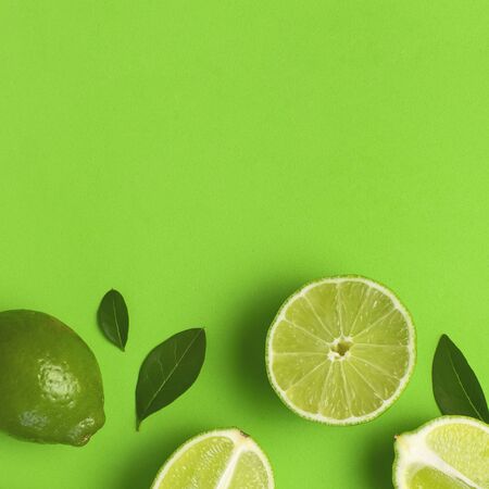 Fresh juicy lime and green leaves on bright green background. Top view flat lay copy space. Creative food background, tropical fruit, vitamin C, citrus. Composition with whole and slices of lime.の写真素材