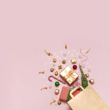 New Year Christmas composition. Paper bag and holiday decorations golden gift Christmas balls fir branches confetti Candy Cane on pink background Flat lay top view copy space Winter New Year 2020 Xmas.の写真素材