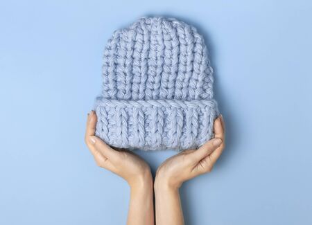 Flat lay fashionable blue knitted winter hat in female hands on blue background top view. Stylish woolen hat, concept of winter accessories for the cold. Advertising, shopping, winter sale.の写真素材