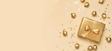 Merry Christmas and Happy Holidays greeting card. Beautiful golden gift with balls and confetti stars on gold background top view Flat lay. New Year presents Festive decorations 2020 celebration.の写真素材