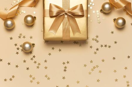 Merry Christmas and Happy Holidays greeting card. Beautiful golden gift balls ribbons confetti stars on gold background top view Flat lay. New Year presents Festive decorations 2020 celebration.の写真素材