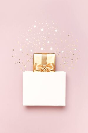 Beautiful golden gift white paper bag confetti stars on pink background top view Flat lay. New Year presents Festive decorations 2020 celebration. Merry Christmas and Happy Holidays greeting card.の写真素材