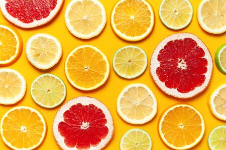 Flat lay composition with slices of fresh lemon orange grapefruit lime on yellow background top view. Citrus Juice Concept, Vitamin C, Fruits. Creative summer background. Close-up fruit pattern.の写真素材