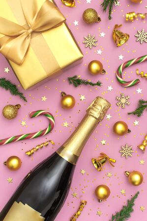 Christmas and New Year background. Champagne bottle, golden gift, christmas balls, festive ribbons, fir branches, star confetti on pink background top view. Flat lay holiday card. Festive decorations.の写真素材