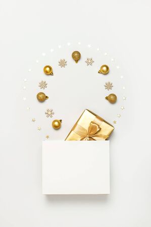 Beautiful golden gift white paper bag confetti stars Christmas balls on gray background top view Flat lay. New Year presents Festive decorations 2020 celebration. Merry Christmas Happy Holidays card.の写真素材