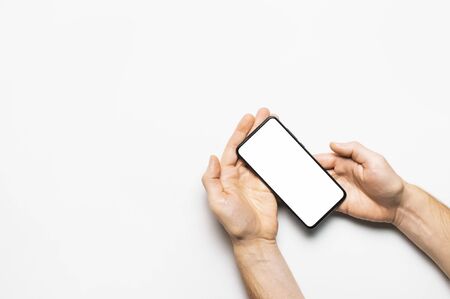 Male hands hold a modern black smartphone with white blank screen on light gray background. Modern technology, phone, gadget in hands, touch screen, template for your design. Mockup.の写真素材