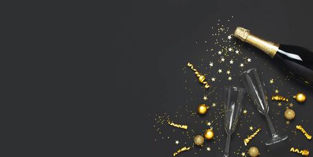 Christmas and New Year background. Champagne bottle champagne glasses golden christmas balls festive ribbons star confetti on black background top view. Flat lay holiday card. Party decorations 2020.の写真素材