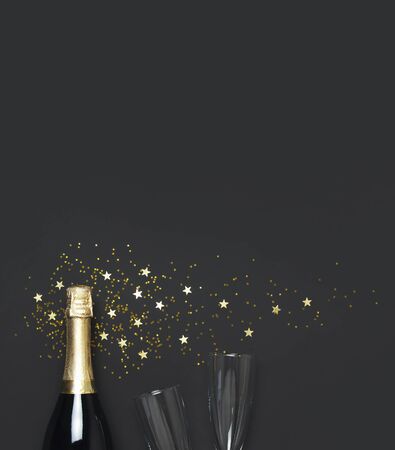 Christmas and New Year background. Champagne bottle, champagne glasses, festive golden star confetti on black background top view. Flat lay holiday card. Birthday or party concept. Festive decorations.の写真素材