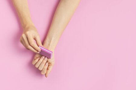 Stylish beautiful gentle manicure. Hands of young woman with nail file on pink background top view flat lay copy space. Natural nails, gel polish, self-care, beauty and fashion. Nail care salon spa.の写真素材
