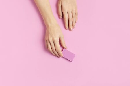 Stylish beautiful gentle manicure. Hands of young woman with nail file on pink background top view flat lay copy space. Natural nails, gel polish, self-care, beauty and fashion. Nail care salon spa.の写真素材
