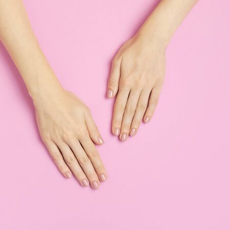 Stylish beautiful gentle manicure. Hands of young woman on pink background top view flat lay copy space. Natural nails, gel polish, self-care, beauty and fashion. Nail care, Beauty salon advertisement.の写真素材