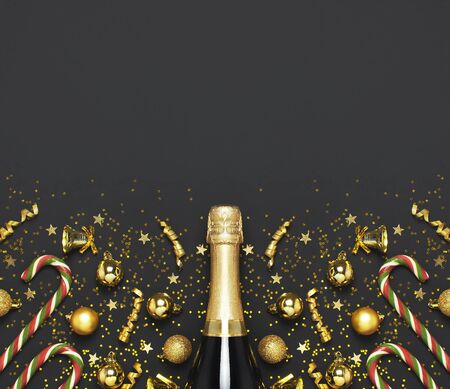 Christmas and New Year background. Champagne bottle, golden christmas balls, festive ribbons, star confetti on black background top view. Flat lay holiday card. Party concept Festive decorations 2020.の写真素材