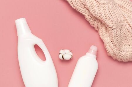 Eco cleaning concept. White plastic packaging of laundry detergent, liquid powder, washing conditioner, knitted wool sweater, cotton flowers on pink background. Flat lay top view. Bio organic product.の写真素材