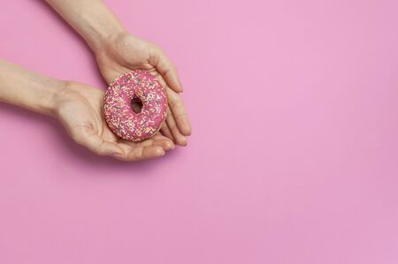 Beautiful female hands with gentle manicure hold sweet donut on pink background top view flat lay copy space. Natural nails, gel polish, self-care, beauty and fashion. Nail care. Donut Background.の写真素材