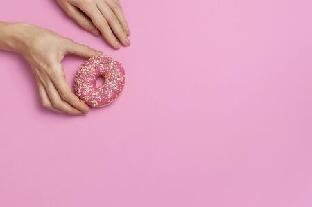 Beautiful female hands with gentle manicure hold sweet donut on pink background top view flat lay copy space. Natural nails, gel polish, self-care, beauty and fashion. Nail care. Donut Background.の写真素材
