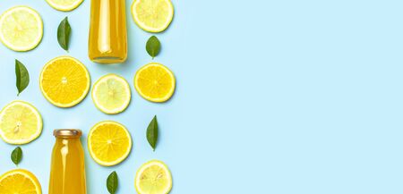 Flat lay composition with glass bottles of juice or fresh, slices of fresh lemon and orange, green leaves, ice cubes on blue background top view copy space. Citrus Juice Concept, Vitamin C, Fruits.の写真素材