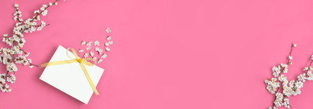 White gift bag with gold ribbon and branch of spring white flowers on bright pink background....
