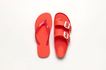 Fashionable beach coral flip flops and sandals on white background. Flat lay, top view, copy space. Creative beach concept, stylish summer shoes, vacation, travel. Trend coral color.の写真素材
