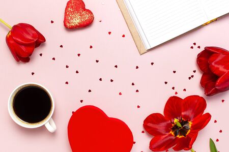 Red tulips, red heart shaped gift box, cup of coffee, blank notebook, macaron cake, confetti on pastel pink background top view Flat lay. Mother's Day Valentines Day birthday holiday background.の写真素材